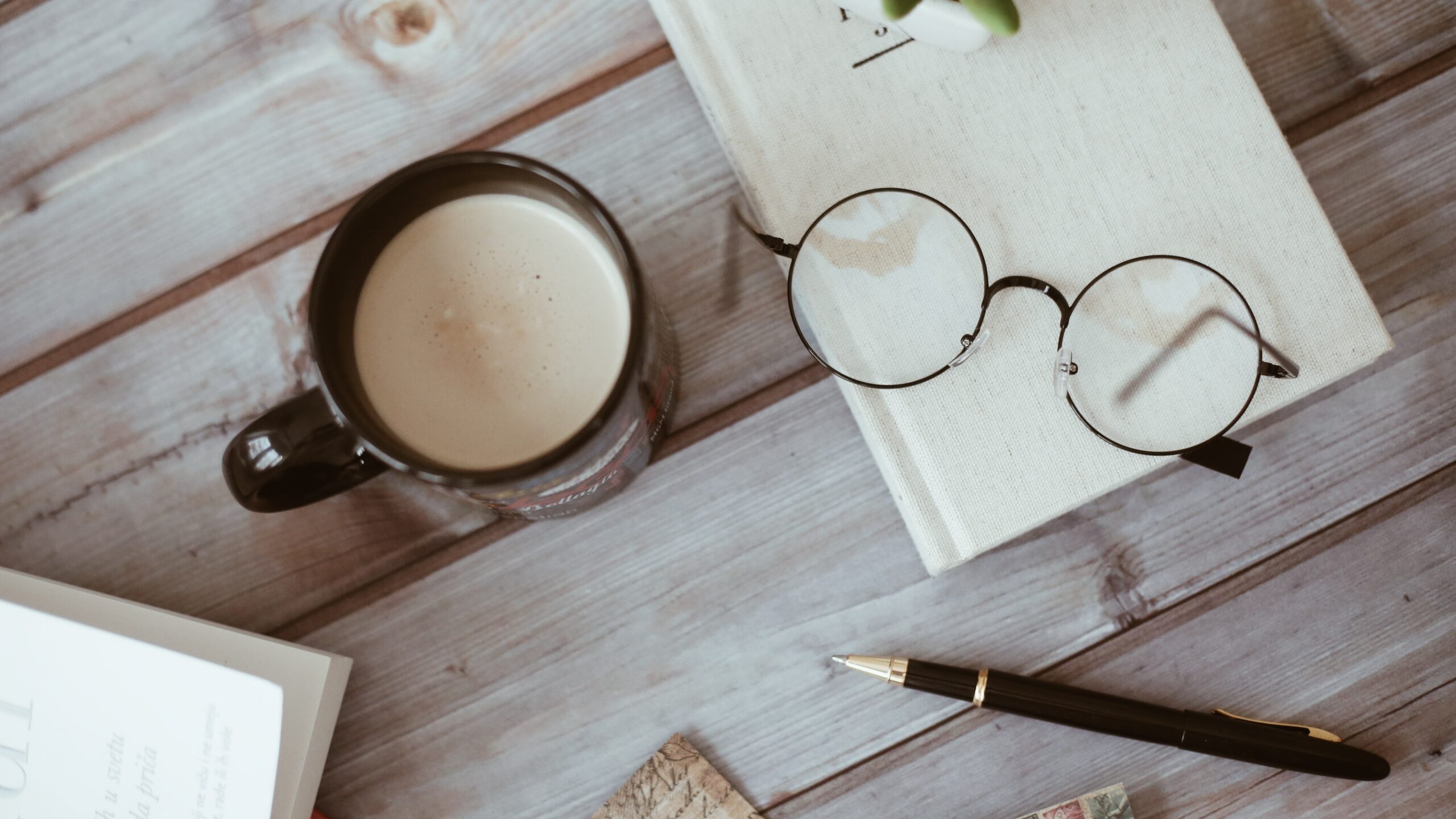 mesa com café com leite, óculos, caneta e planar literário para o momento da leitura