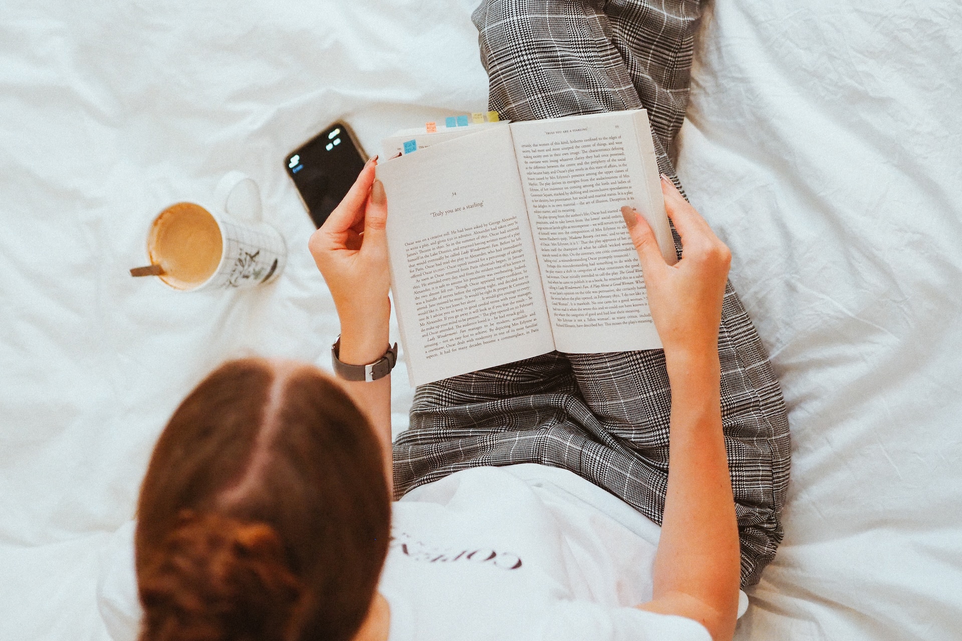 menina sentada na cama lendo um livro com celular ao lado para auxiliar com o cronômetro com o intuito de focar em sua leitura durante o tempo estipulado do método pomodoro